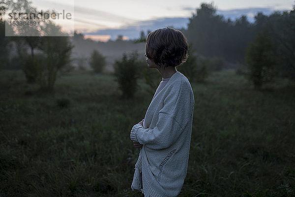 Junge Frau in weißer Strickjacke auf einem Feld bei Sonnenuntergang
