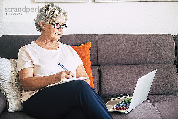 Ältere Frau mit Stift und Laptop auf dem Sofa
