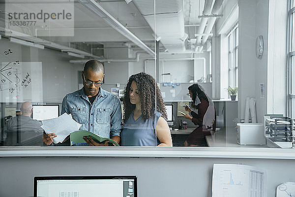 Blick durch das Fenster auf Mitarbeiter  die im Büro Dokumente lesen