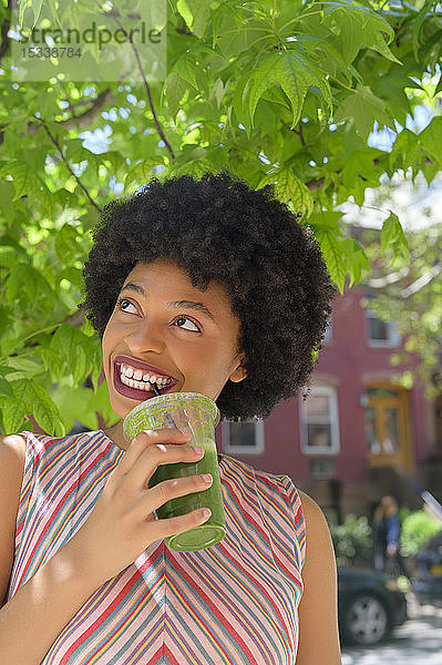 Frau trinkt grünen Saft unter einem Baum
