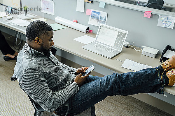Mann mit hochgelegten Füßen bei der Nutzung eines Smartphones im Büro