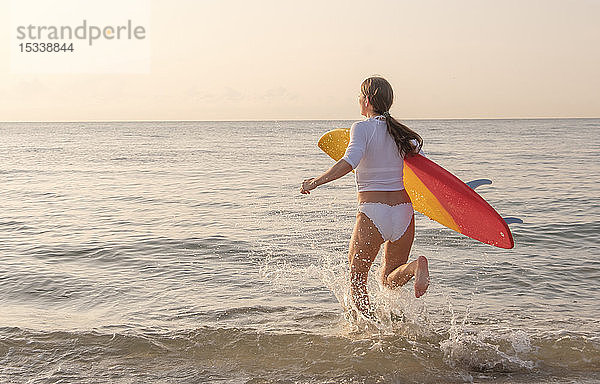 Frau hält Surfbrett und läuft ins Meer
