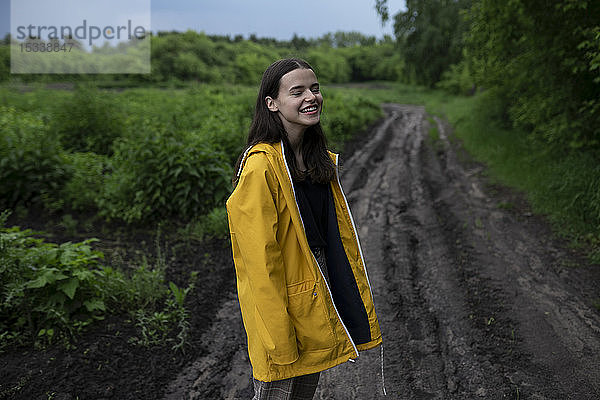 Lächelndes Teenager-Mädchen mit gelbem Regenmantel auf einer Landstraße