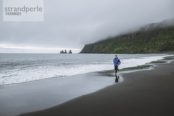 Mann joggt am Strand in Vik  Island