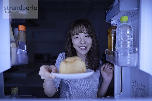 Junge Japanerin isst Nachtsnack aus dem Kühlschrank