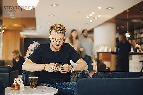 Mittelgroßer erwachsener Mann benutzt Smartphone  während er im Restaurant sitzt