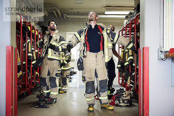 Feuerwehrmänner schauen auf  während sie Arbeitsschutzkleidung in der Umkleidekabine der Feuerwache tragen