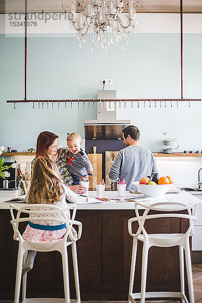Frau sieht den Sohn an  während sie neben der Tochter steht  die in der Küche lernt