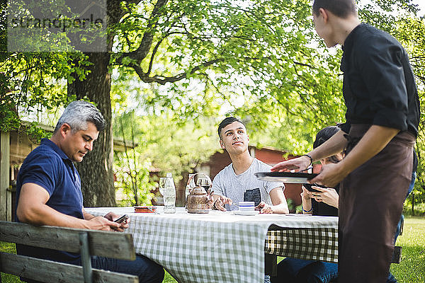 Teenager  der den Kellner ansieht  während er mit Freunden im Restaurant sitzt