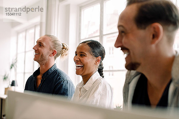 Kreative Geschäftskollegen lächeln beim Wegschauen im Büroraum