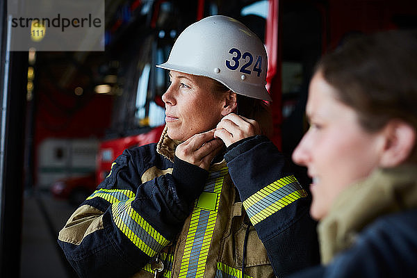 Weibliche Feuerwehrfrau mit Helm  während sie mit einem Mitarbeiter in der Feuerwache steht