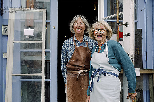 Porträt von fröhlichen älteren Besitzerinnen  die am Eingang des Geschäfts stehen