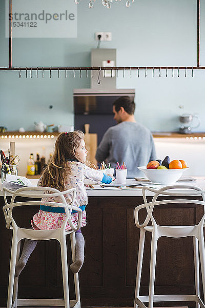 Rückansicht eines Mädchens  das weg schaut  während es auf einer Kücheninsel sitzt  während der Vater im Hintergrund steht