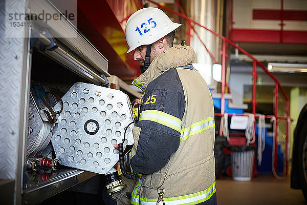 Seitenansicht eines Feuerwehrmannes  der den Feuerwehrschlauch im Löschfahrzeug auf der Station anordnet