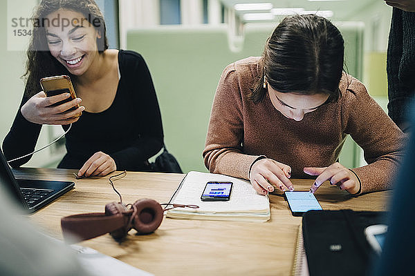 Gymnasiastinnen mit Smartphone am Schreibtisch im Klassenzimmer