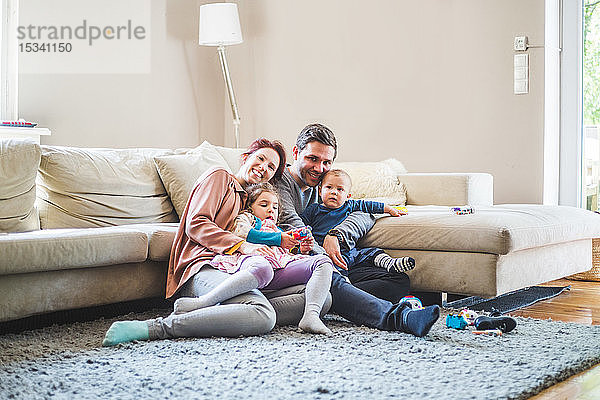 Porträt von glücklichen Eltern  die mit ihren Kindern zu Hause im Wohnzimmer sitzen