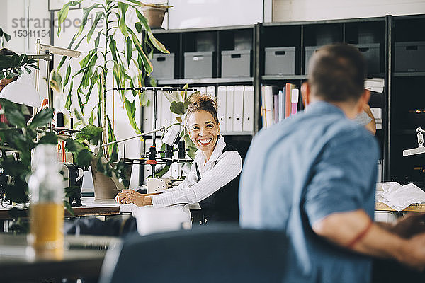 Lächelnde Geschäftsfrau schaut einen männlichen Kollegen an  während sie in einem kreativen Büro arbeitet