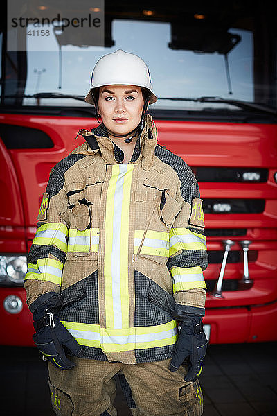Porträt eines selbstbewussten Feuerwehrmannes  der vor dem Feuerwehrauto in der Feuerwache steht