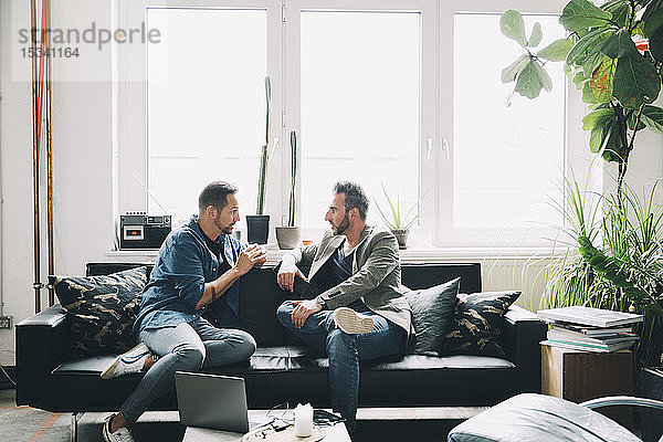 Selbstbewusste männliche Kollegen diskutieren auf dem Sofa sitzend im Kreativbüro