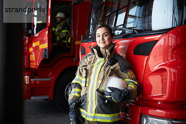 Porträt einer selbstbewussten Feuerwehrfrau  die in der Feuerwache am Löschfahrzeug steht