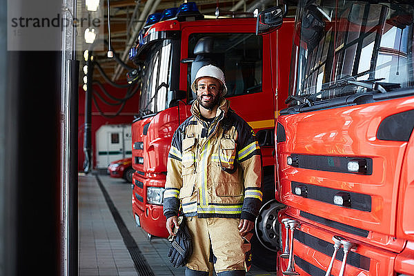 Porträt eines lächelnden Feuerwehrmannes  der in der Feuerwache beim Löschfahrzeug steht