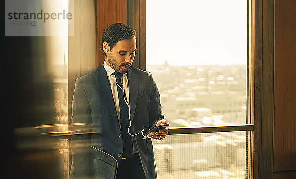 Mittlerer erwachsener Jurist  der ein Smartphone benutzt  während er in einer Anwaltskanzlei am Fenster steht