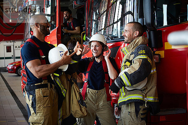 Fröhliche Feuerwehrleute diskutieren  während sie in der Feuerwache beim Löschfahrzeug stehen
