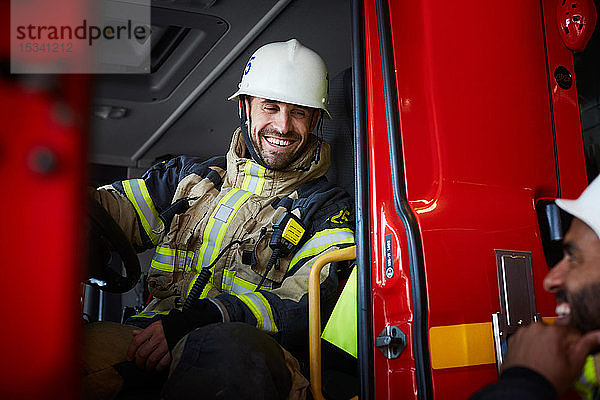 Lächelnder Feuerwehrmann sitzt im Feuerwehrauto  während er mit seinem Kollegen spricht