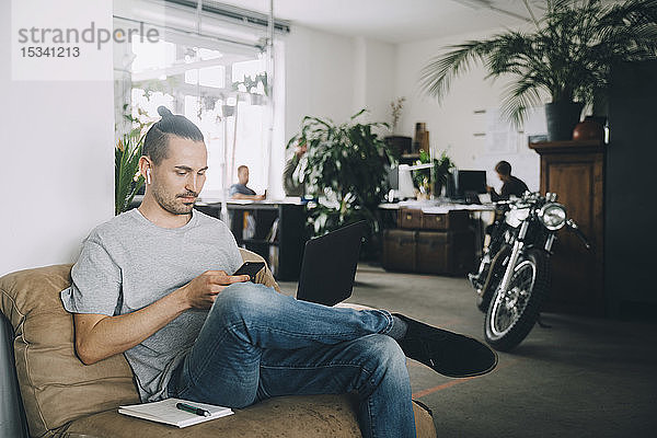 Selbstbewusster Geschäftsmann nutzt Technologien  während er im kreativen Büro sitzt