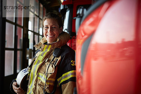 Porträt einer lächelnden Feuerwehrfrau  die in der Feuerwache beim Löschfahrzeug steht