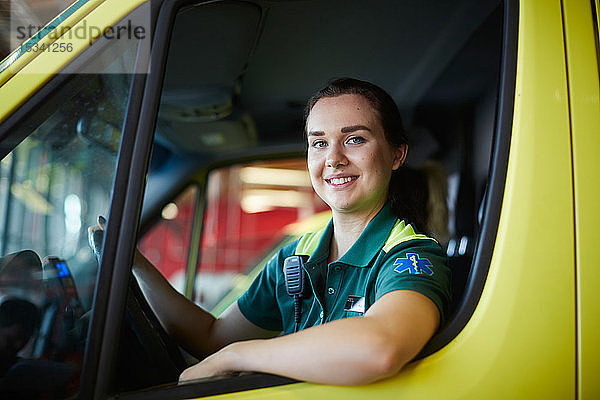 Porträt einer lächelnden jungen Sanitäterin  die einen Krankenwagen auf einem Parkplatz fährt