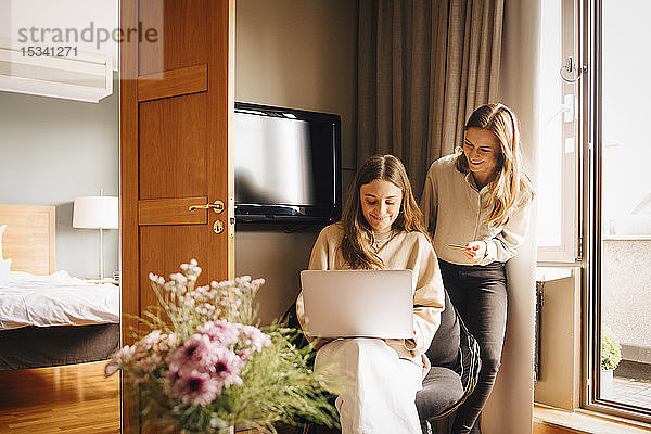 Glückliche Freunde  die während der Ferien online mit Kreditkarte per Laptop im Hotelzimmer einkaufen