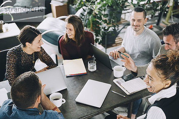 Schrägansicht von glücklichen Geschäftsleuten  die in einem kreativen Büro am Tisch sitzen