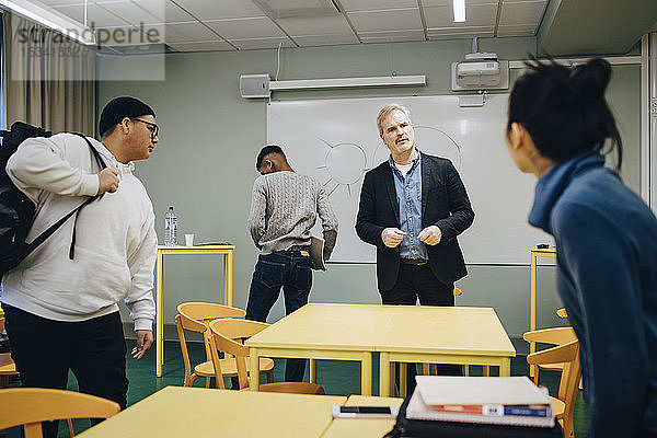 Männlicher Lehrer spricht mit einer Schülerin  die im Klassenzimmer steht