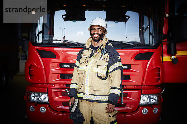 Porträt eines lächelnden Feuerwehrmannes in Uniform  der in der Feuerwache vor dem Feuerwehrauto steht
