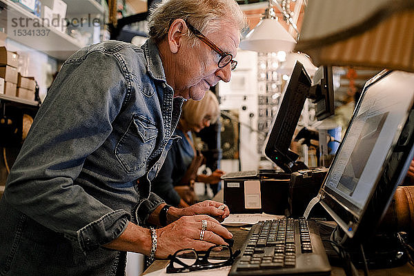 Seitenansicht eines selbstbewussten Verkäufers in Denim-Hemd am Computer an der Kasse eines Baumarktes