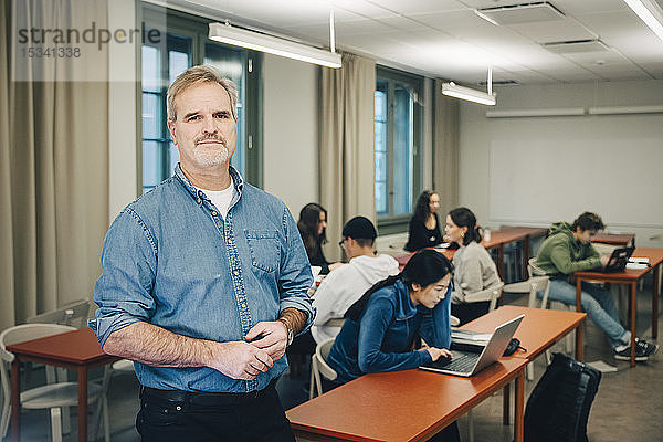 Porträt eines männlichen Lehrers mit Studenten  die am Schreibtisch im Klassenzimmer lernen
