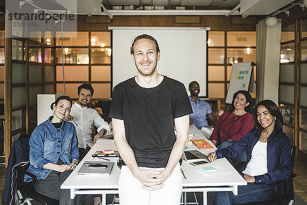 Porträt eines lächelnden Geschäftsmannes  der mit dem Team im Hintergrund im Sitzungssaal steht