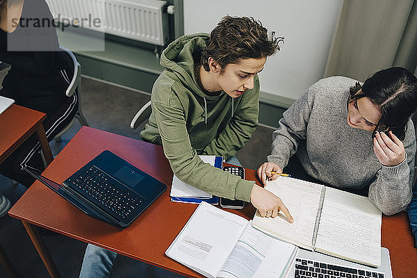 Hochwinkelansicht eines männlichen Studenten  der einer Klassenkameradin am Schreibtisch im Klassenzimmer assistiert