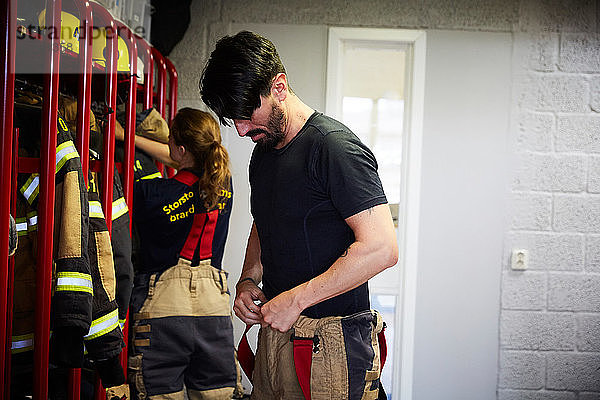 Männliche und weibliche Feuerwehrmänner und -frauen tragen Arbeitsschutzkleidung in der Umkleidekabine der Feuerwache