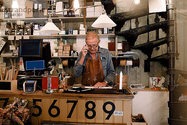 Selbstbewusster älterer männlicher Unternehmer arbeitet  während er an der Kasse im Laden steht