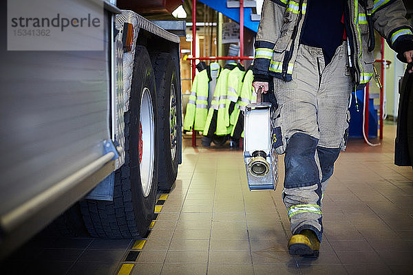 Niedriger Abschnitt eines Feuerwehrmannes  der einen Feuerwehrschlauch hält  während er in der Feuerwache geht