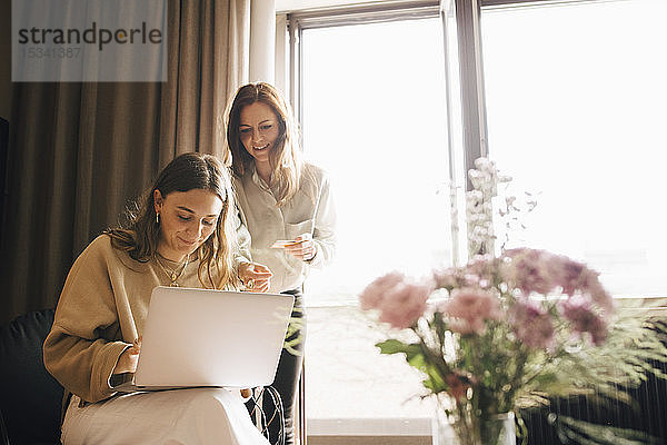 Lächelnde Freunde beim Online-Shopping mit Kreditkarte über Laptop im Hotelzimmer