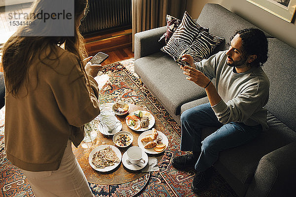 Hochwinkelaufnahme eines Paares  das das Frühstück im Hotelzimmer fotografiert