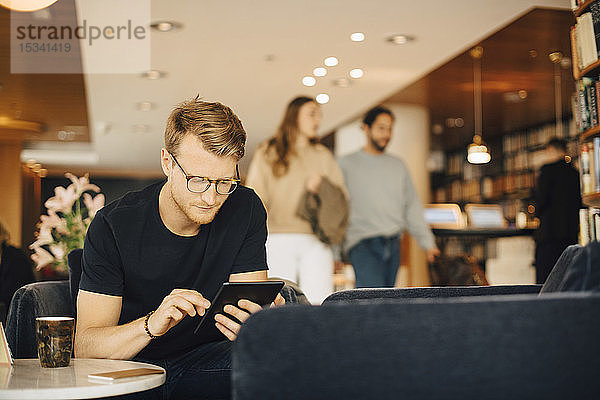 Mittlerer erwachsener Mann benutzt digitales Tablet  während er am Wochenende im Restaurant sitzt