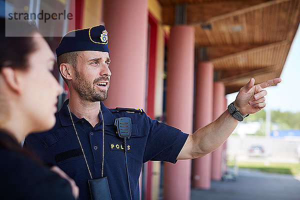 Männlicher Polizeibeamter zeigt auf einen Mitarbeiter vor einer Polizeistation  während er diesen anweist