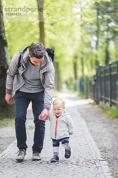 Vater und Sohn halten sich beim Gehen auf dem Fußweg in voller Länge an den Händen