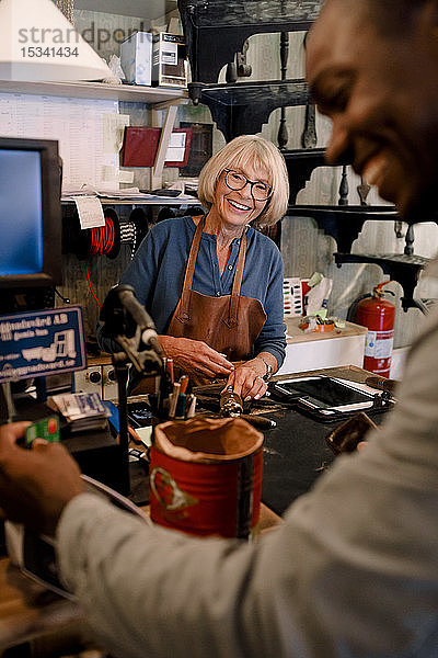 Fröhliche ältere Verkäuferin betrachtet männlichen Kunden  der im Baumarkt mit Kreditkarte bezahlt