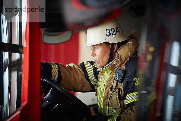 Weibliche Feuerwehrfrau mit Helm sitzt im Feuerwehrwagen auf der Feuerwache