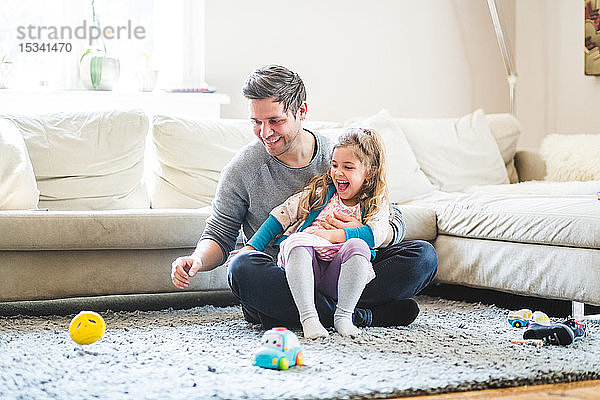 Fröhliche Vater und Tochter schauen sich Spielzeug an  während sie zu Hause spielen